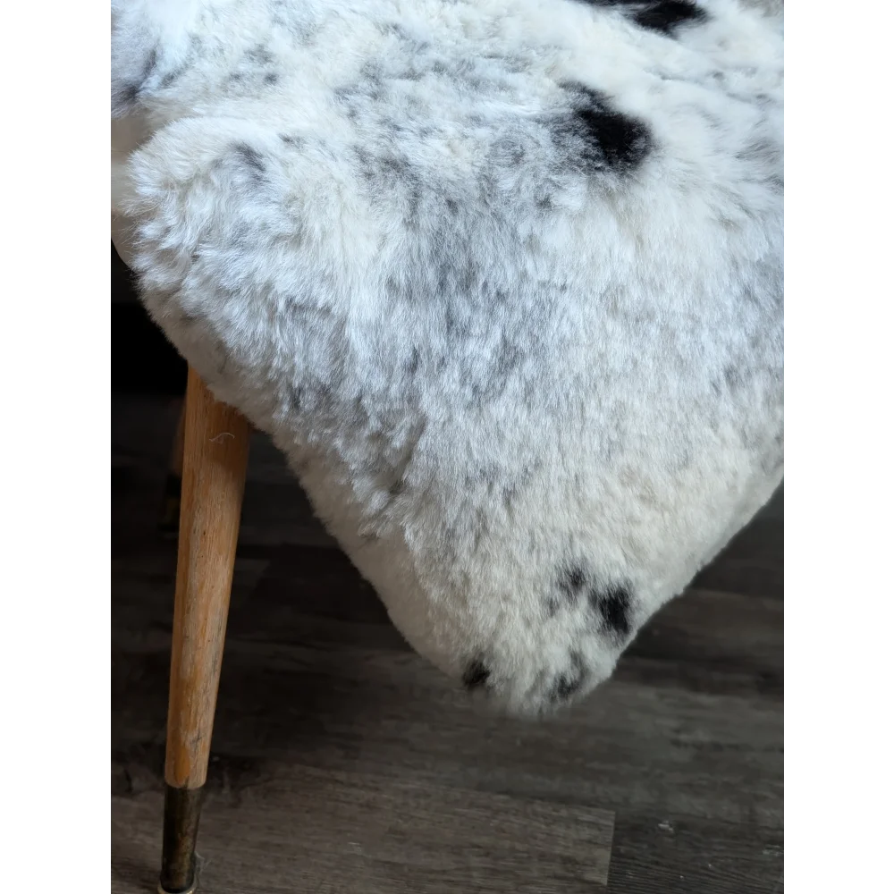 A plush white and black spotted icelandic sheepskin rug draped over a wooden leg showcasing medium spotted icelandic wool
