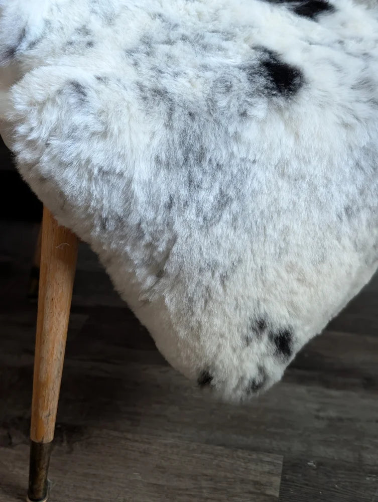 A plush white and black spotted icelandic sheepskin rug draped over a wooden leg showcasing medium spotted icelandic wool