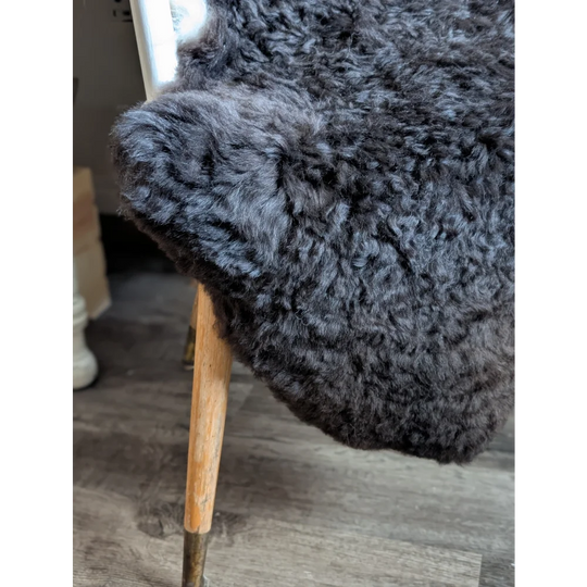 A plush large soft blacky icelandic sheepskin throw with dark gray curly fur draped over a wooden chair leg