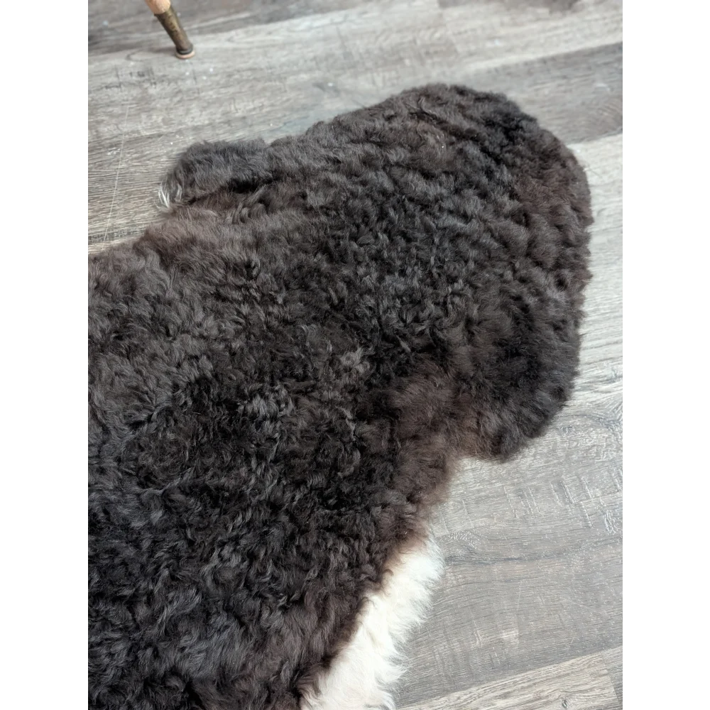 A plush dark gray large icelandic sheepskin rug with white edge made of soft short wool on wooden floor