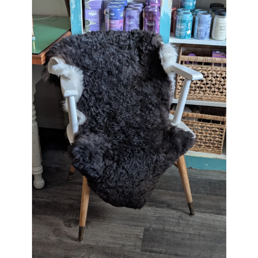 Dark gray fluffy icelandic sheepskin rug with white fur trim draped over vintage wooden chair perfect for cozy decor