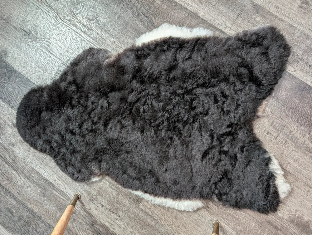 A large soft blacky icelandic sheepskin rug with short wool and natural irregular edges in dark gray and white tones