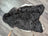 A large soft blacky icelandic sheepskin rug with short wool and natural irregular edges in dark gray and white tones