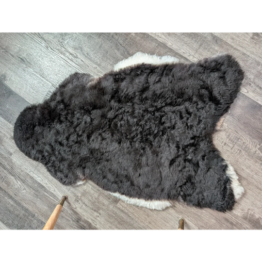 A large soft blacky icelandic sheepskin rug with short wool and natural irregular edges in dark gray and white tones