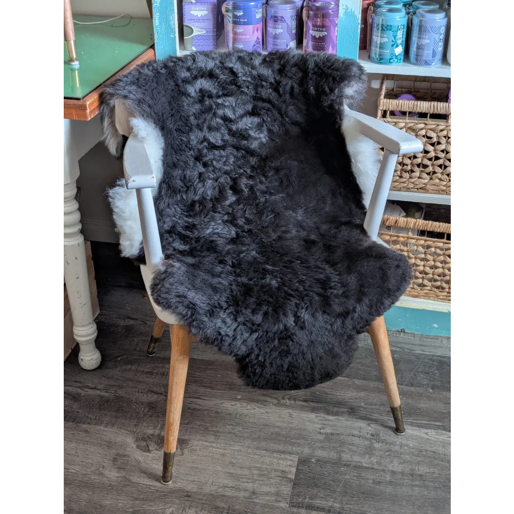 A large soft blacky icelandic sheepskin rug with short wool draped over a white wooden chair seat and back