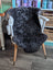 A large soft blacky icelandic sheepskin rug with short wool draped over a white wooden chair seat and back