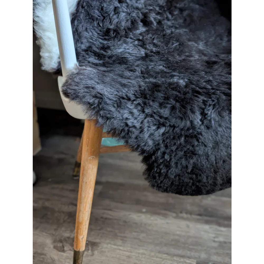 A plush dark gray icelandic sheepskin rug with short wool draped over a wooden chair leg for cozy decor