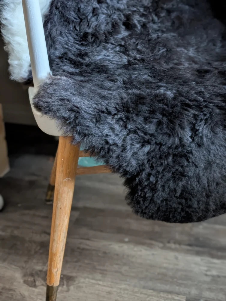 A plush dark gray icelandic sheepskin rug with short wool draped over a wooden chair leg for cozy decor