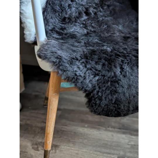 A plush dark gray icelandic sheepskin rug with short wool draped over a wooden chair leg for cozy decor