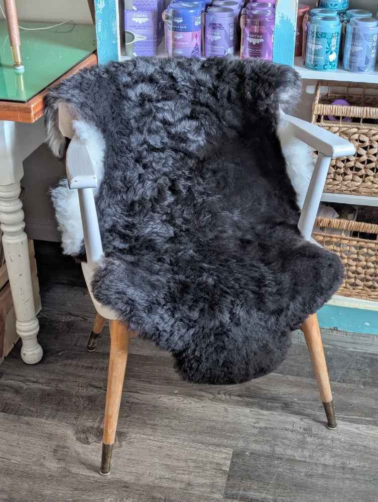 A plush dark gray icelandic sheepskin rug with short wool draped over a white wooden chair with tapered legs