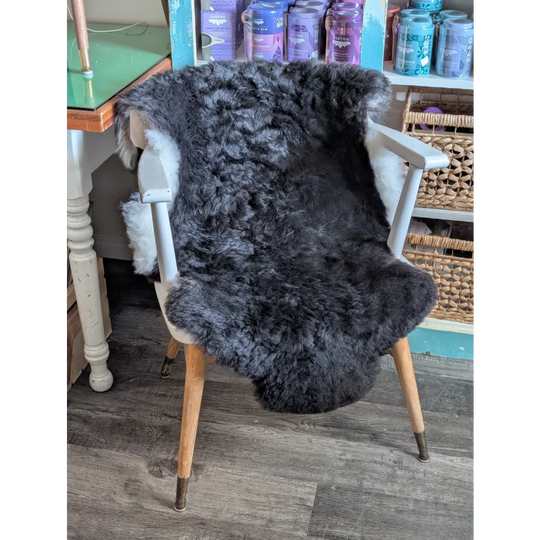 A plush dark gray icelandic sheepskin rug with short wool draped over a white wooden chair with tapered legs