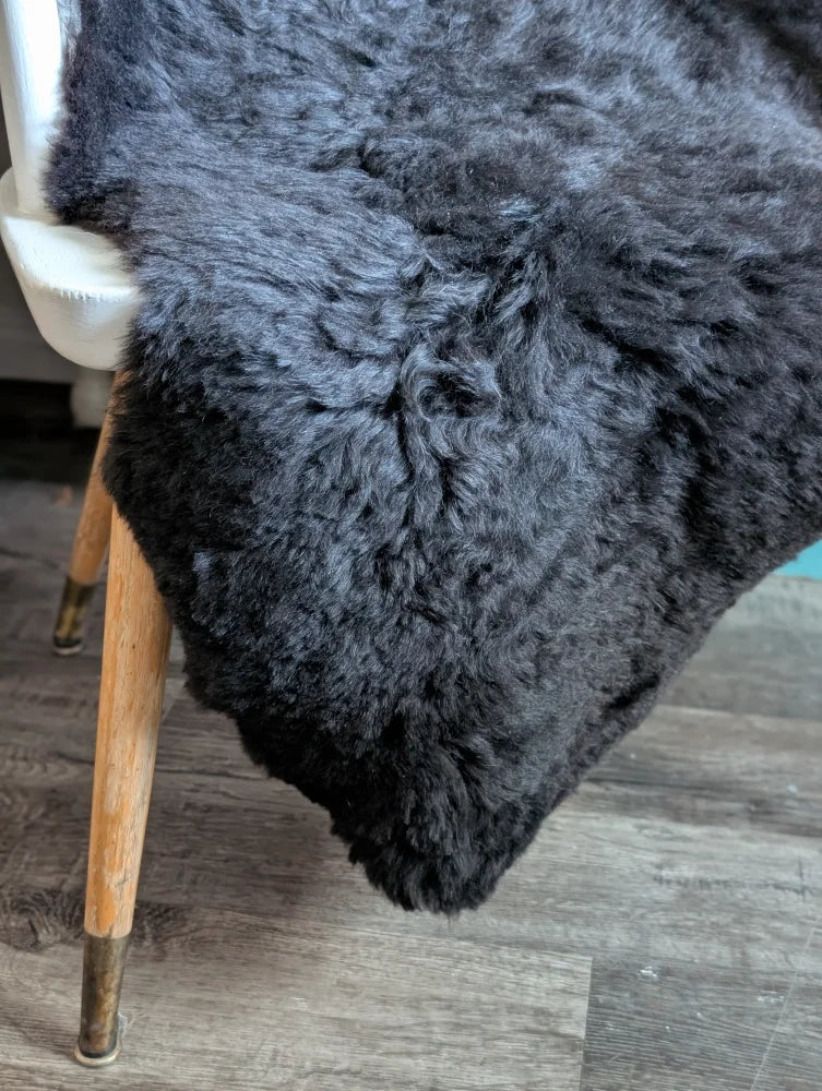 A plush dark gray icelandic sheepskin throw with soft curly short wool draped over the back of a chair