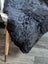 A plush dark gray icelandic sheepskin throw with soft curly short wool draped over the back of a chair