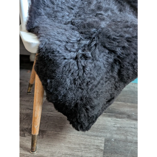 A plush dark gray icelandic sheepskin throw with soft curly short wool draped over the back of a chair