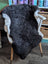 A plush dark gray icelandic sheepskin rug with short wool and white fur trim draped over a wooden chair back