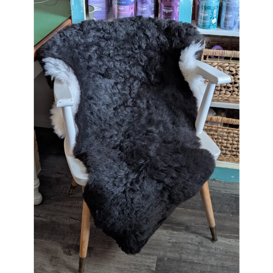 A plush dark gray icelandic sheepskin rug with short wool and white fur trim draped over a wooden chair back
