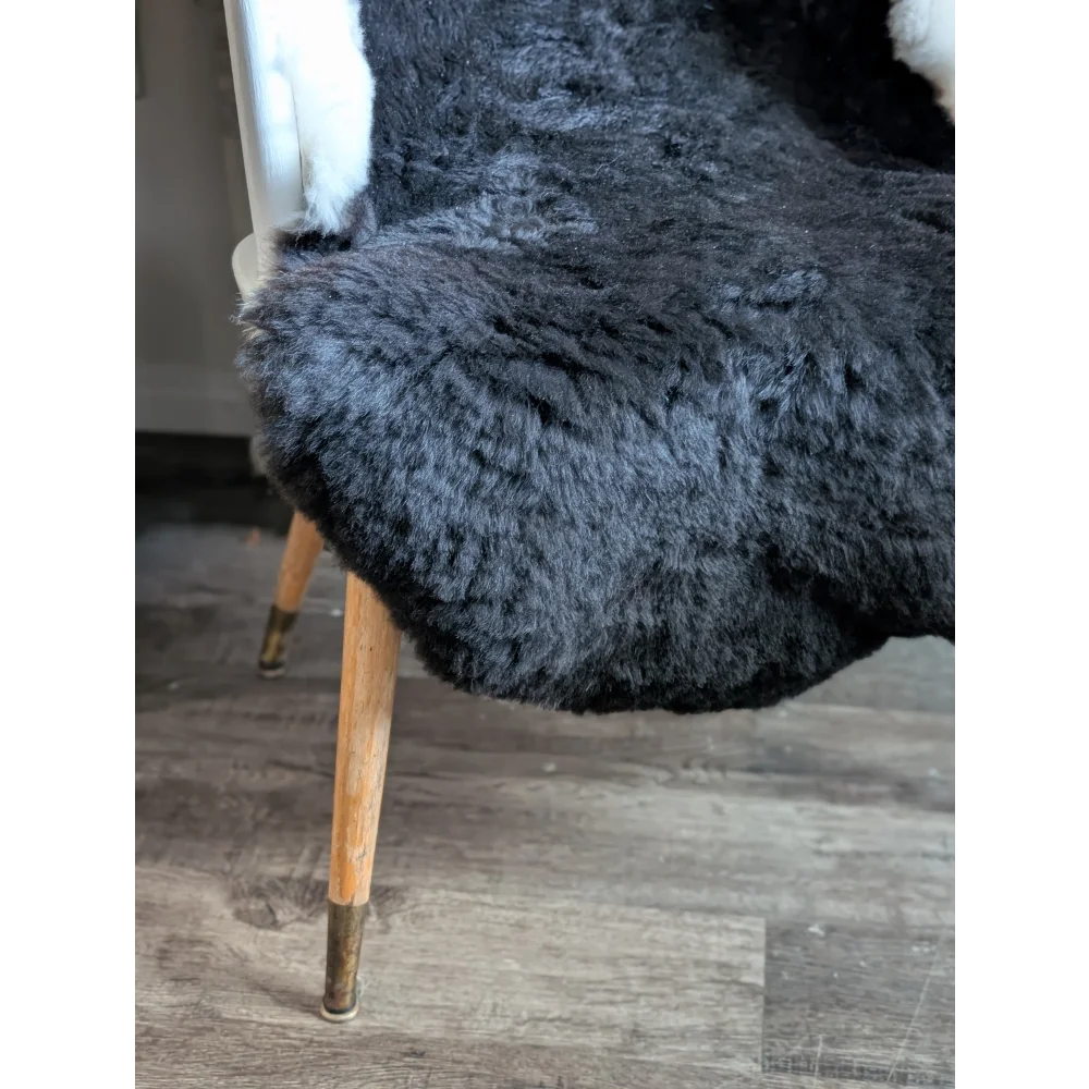 A plush dark gray sheepskin chair with wooden legs and brass caps made from soft blacky icelandic short wool sheepskin