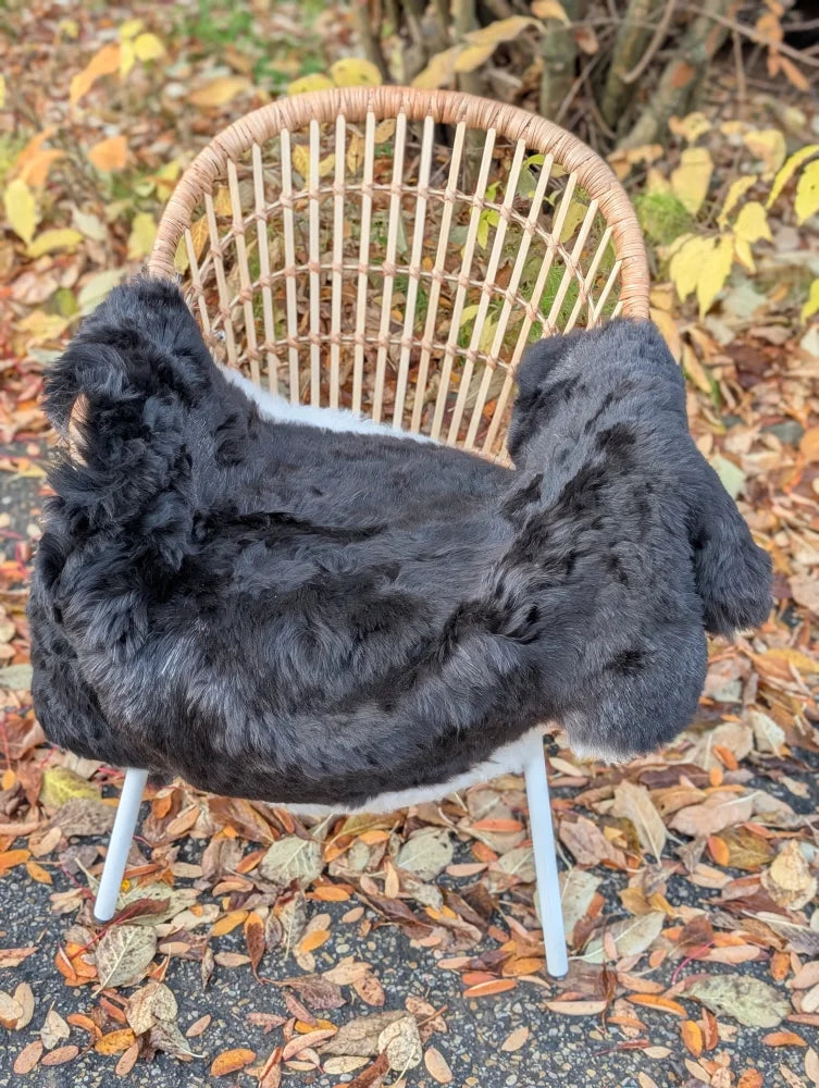 Luv40 black faux fur chair cover draped over wicker chair with white legs featuring wool icelandic sheepskin and dark edges