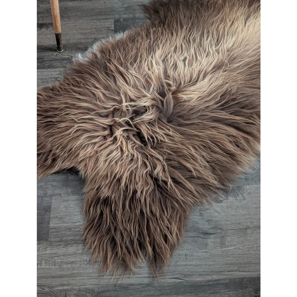 A plush long wool icelandic bronze sheepskin rug with dense fur on a gray wood floor sized 59 by 33 inches