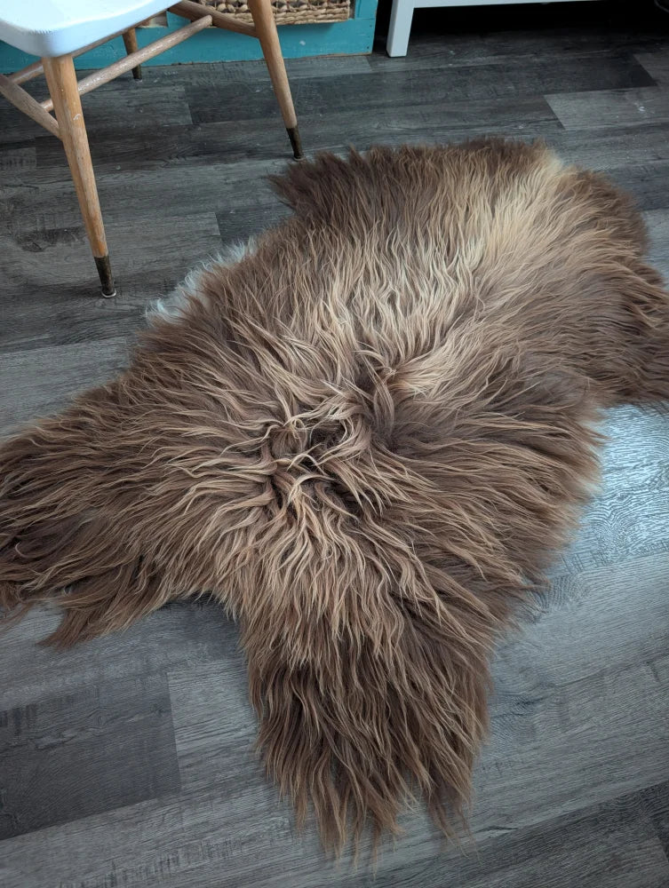 A plush bronze long wool icelandic sheepskin rug with soft fur on a dark wood floor perfect for cozy spaces