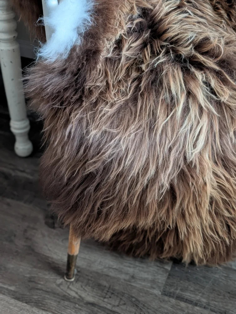 A plush long wool icelandic brown and cream sheepskin-covered stool with wooden legs from luv44 massive bronze collection