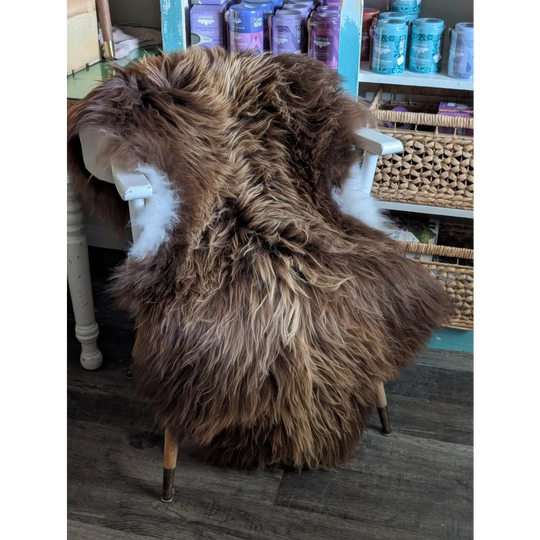 A plush long wool icelandic sheepskin rug in bronze draped over a white wooden chair for cozy decor