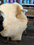 Cream-colored medical sheepskin rug draped over white wooden chair from angus oliver washable sheepskin rugs
