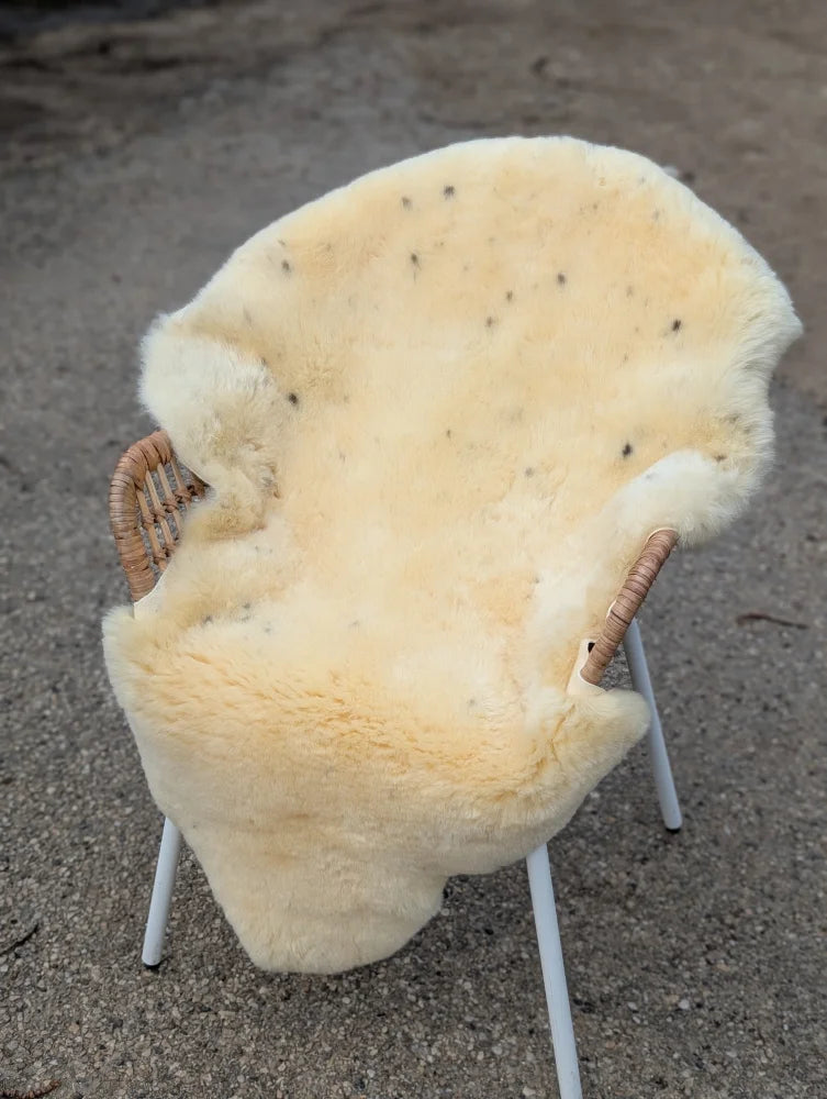 Cream-colored naturally spotted medical sheepskin chair cover with dark speckles on a wicker-backed frame