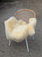 A cozy cream-colored naturally spotted medical sheepskin draped over a woven wicker chair with white metal legs