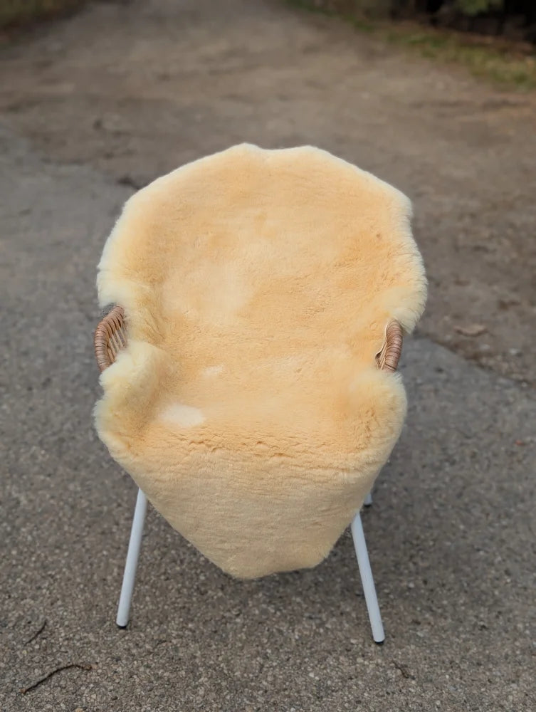 A cozy cream-colored medical sheepskin chair with woven wicker frame and white metal legs from m-10 washable collection