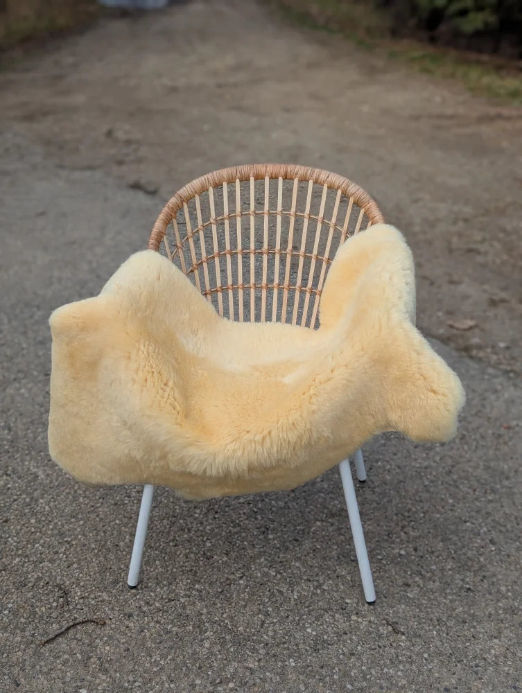A cozy pale yellow medical sheepskin blanket draped over a modern wicker chair with white metal legs
