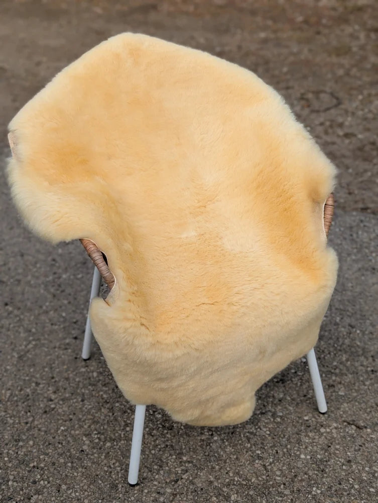 A pale yellow extra large washable medical sheepskin blanket draped over a modern chair with wicker armrests