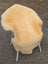 A pale yellow extra large washable medical sheepskin blanket draped over a modern chair with wicker armrests