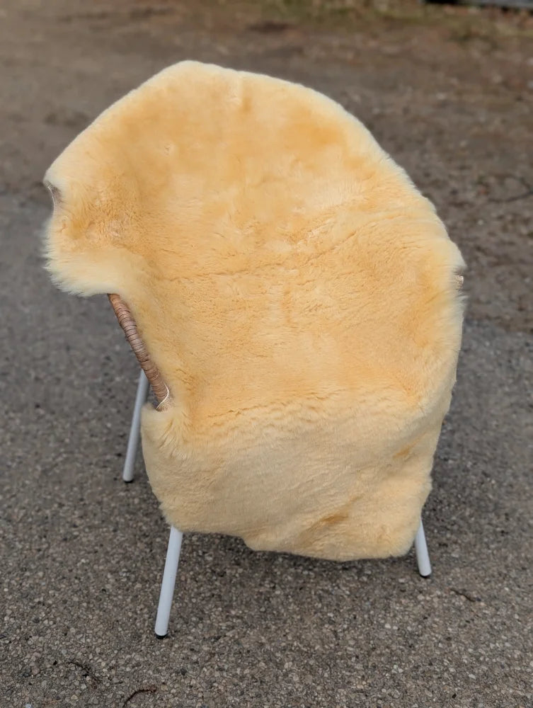 A soft pale yellow extra large washable medical sheepskin blanket draped over a chair with wooden armrests