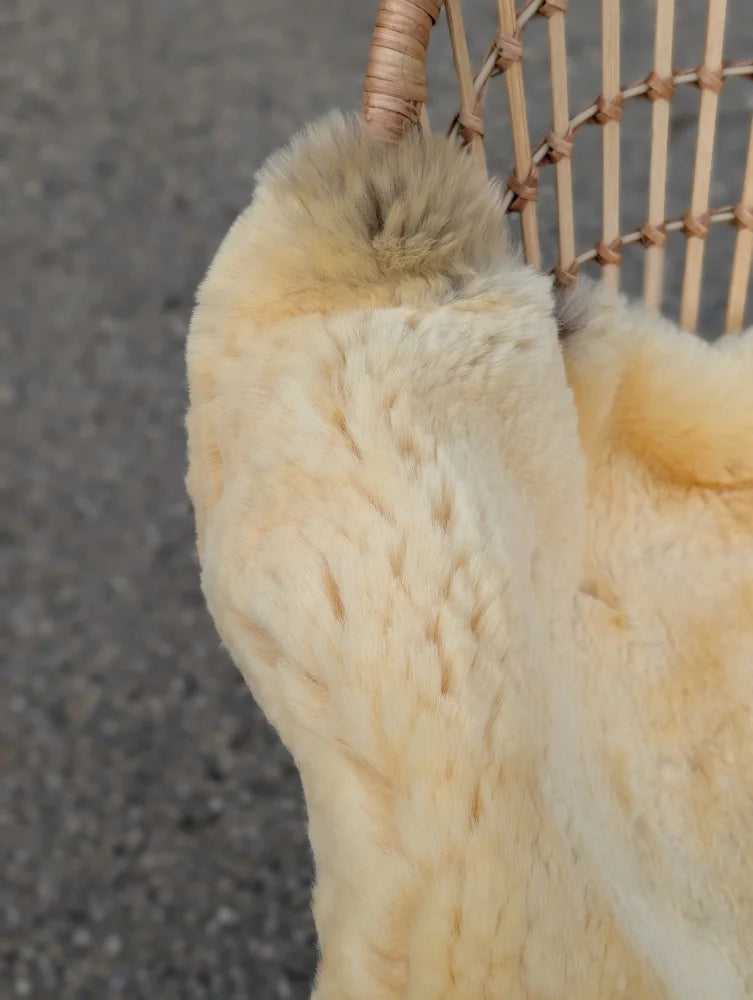 A creamy beige faux fur medical sheepskin draped over a wicker chair naturally spotted and extra large size