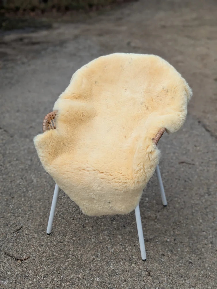 Cream-colored naturally spotted medical sheepskin draped over modern white metal chair with woven armrests