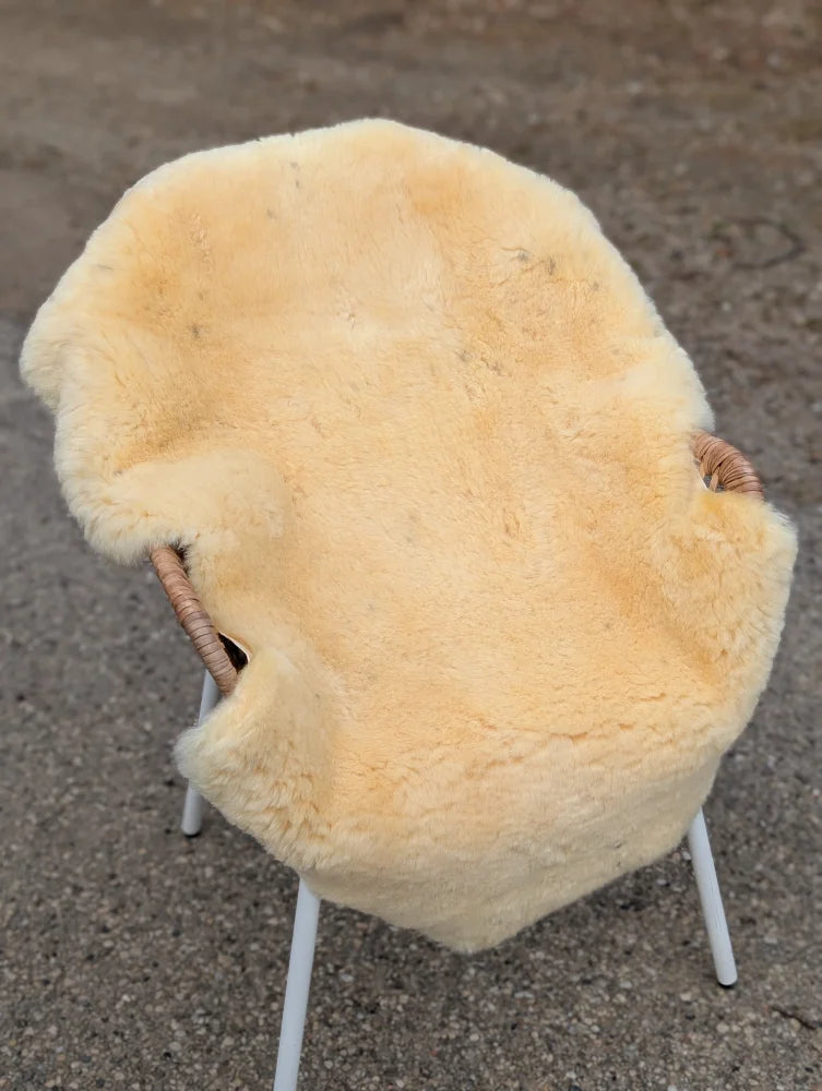 Cream-colored naturally spotted medical sheepskin chair cover on white metal frame with woven wicker armrests