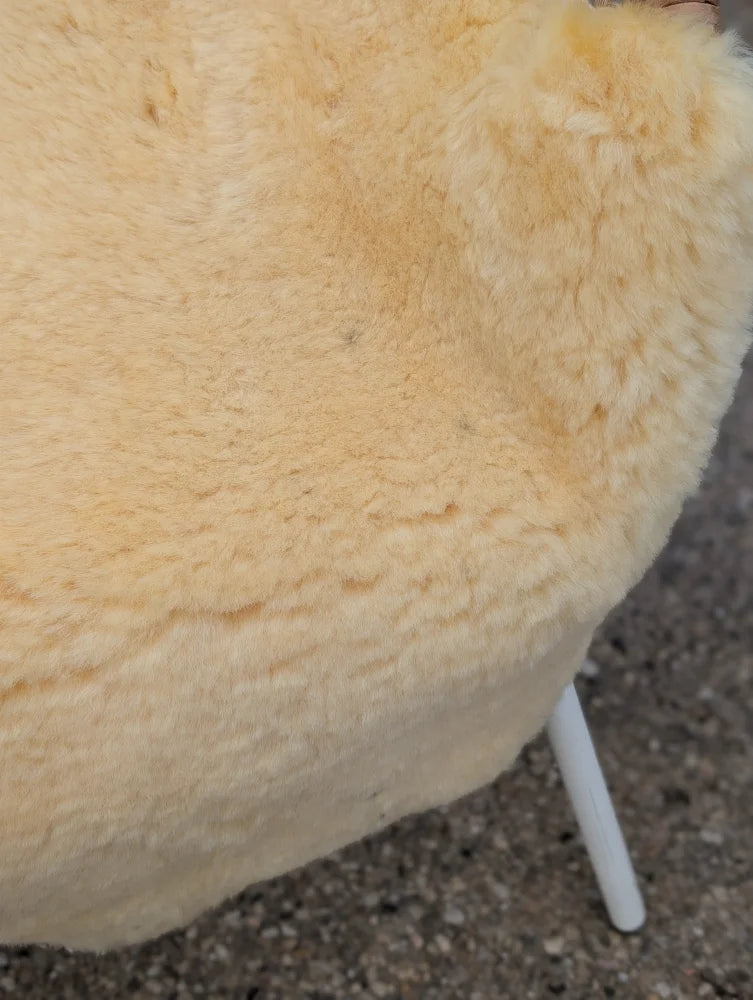 Cream-colored plush sheepskin chair with white metal legs featuring large washable naturally spotted medical sheepskin