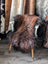 A plush long wool icelandic sheepskin rug in dark rusty brown draped over a white wooden chair with light wood legs