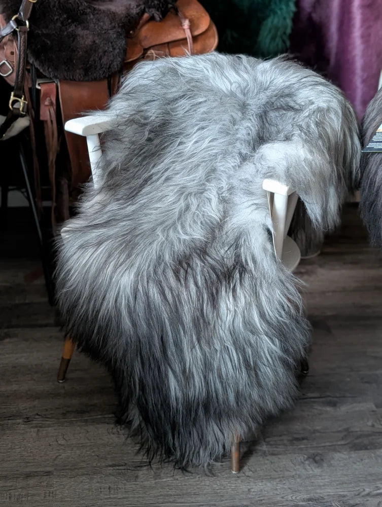 A plush long wool icelandic grey sheepskin rug draped over a white wooden chair for cozy decor
