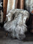 A plush shaggy grey and white long wool icelandic sheepskin draped over a white wooden chair