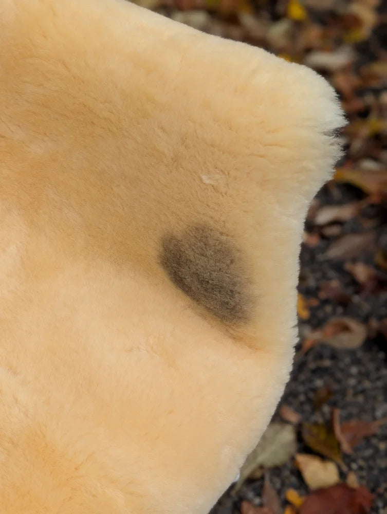 Cream-colored washable medical sheepskin size medium with a dark naturally spotted stain on the shoulder