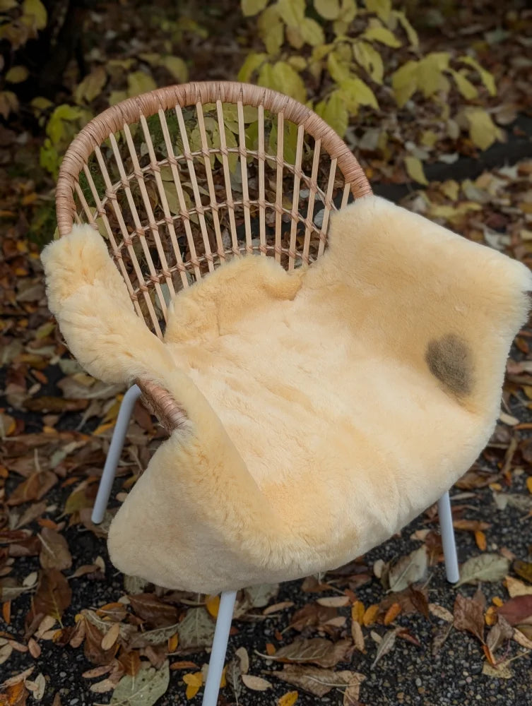 Cream-colored naturally spotted medical sheepskins draped over woven wicker armchair size medium washable cover