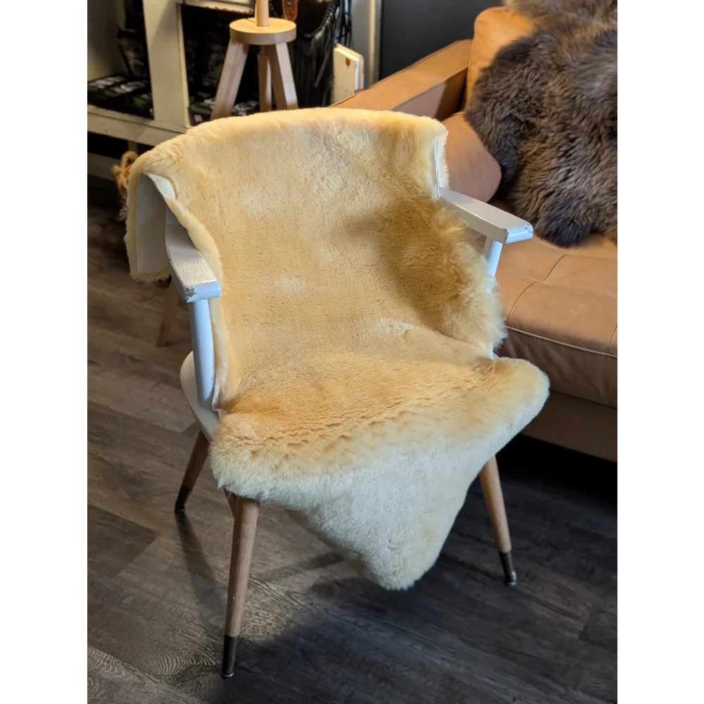 A cozy cream-colored medical sheepskin throw draped over a white wooden armchair with tapered legs by angus oliver