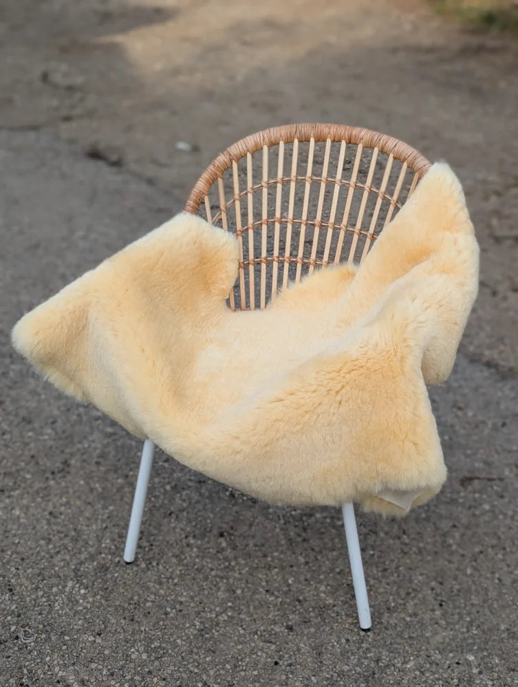 Cream-colored medical sheepskin throw draped over woven rattan chair with white metal legs naturally spotted design
