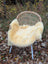 A cozy cream-colored naturally spotted medical sheepskin blanket draped over a wicker chair with blue metal legs