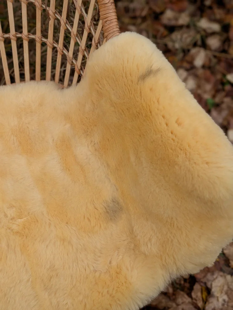 A soft creamy yellow medical sheepskin naturally spotted rug on a woven wicker chair in washable material