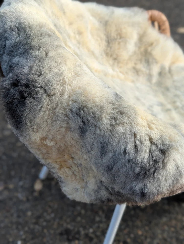 A plush naturally spotted medical sheepskin cushion with soft fluffy texture in gray to white tones for medical use