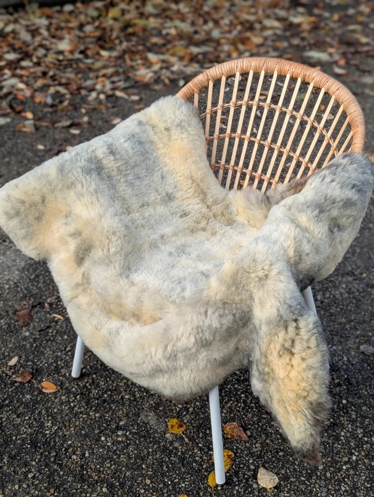 A soft natural-toned medical sheepskin blanket with fluffy texture and naturally spotted grayish-beige color draped on wicker chair