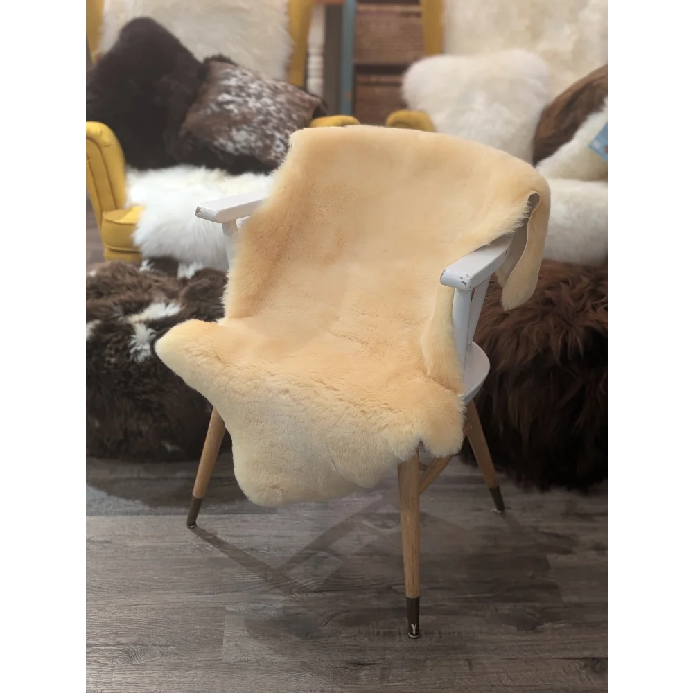 A cozy cream medical sheepskin cover draped over a white wooden chair with light wood legs by angus oliver